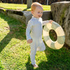Lifestyle image of a toddler running and wearing a full coverage MIKOU green swimsuit on a tropical landscape. 