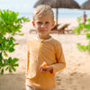 Boy walking on a pristine beach wearing MIKOU orange rash guard